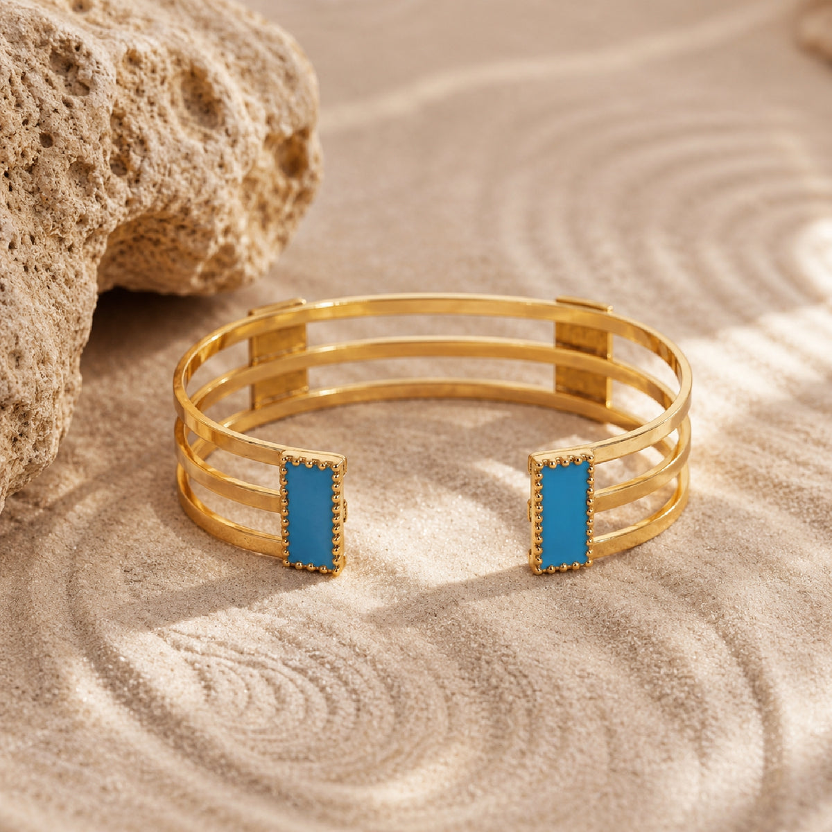 Deco Mosaic 18K gold-plated cuff bracelet in midnight blue and turquoise enamel styled on sand with rock prop — mood shot — Studio Anivarya