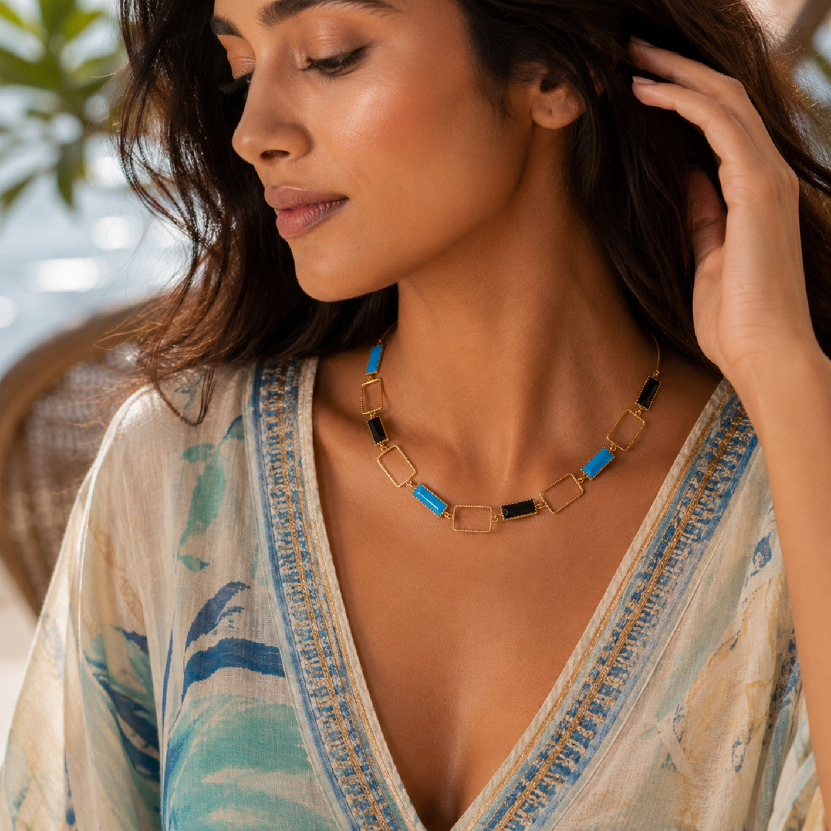 Lifestyle model wearing Deco Mosaic 18K gold-plated princess riviera necklace in black and turquoise blue enamel styled with a kaftan at a resort — Studio Anivarya