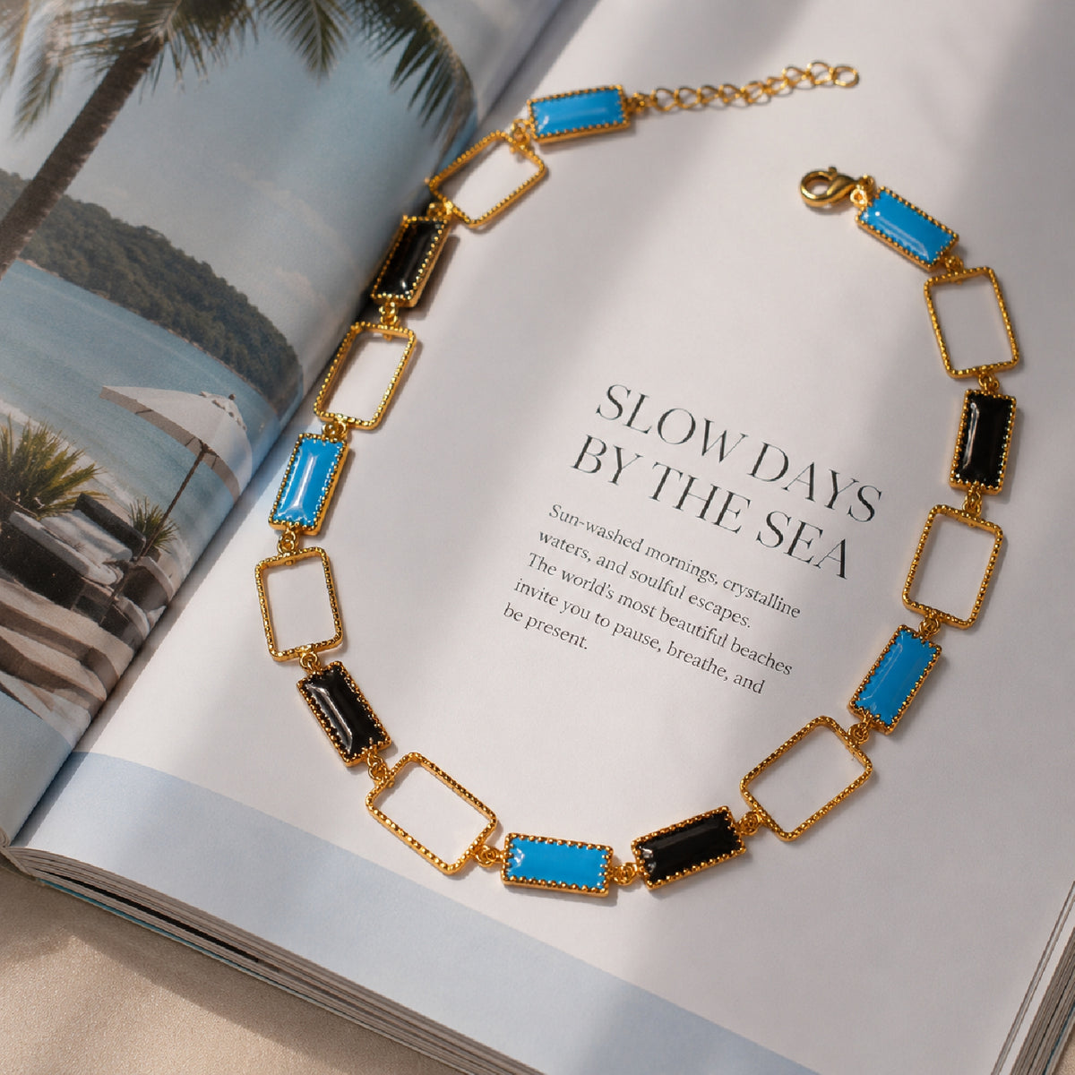 Deco Mosaic 18K gold-plated princess riviera necklace in black and turquoise blue enamel styled in a coastal mood shot with 'Slow Days by the Sea' — Studio Anivarya